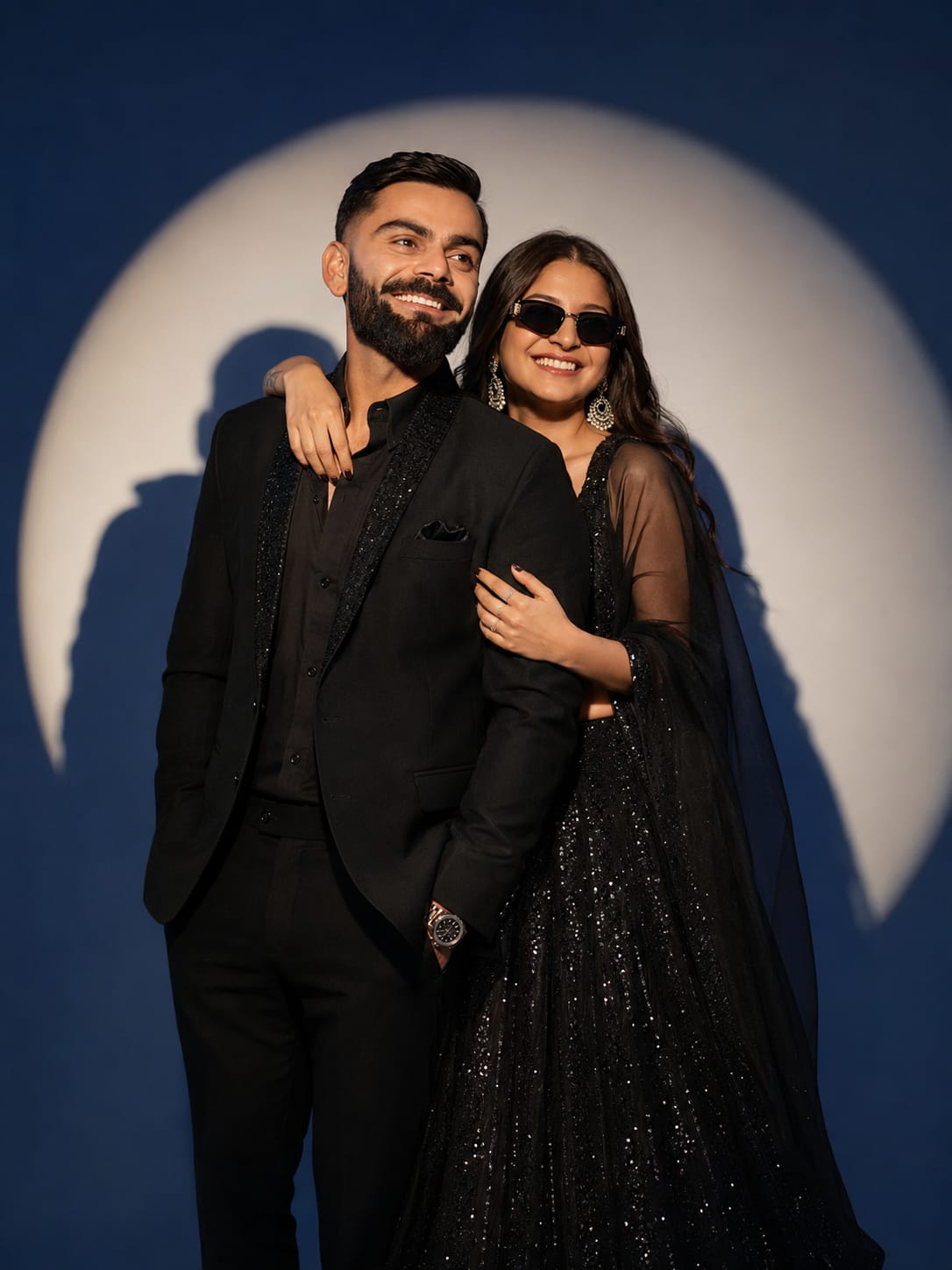 Couple in black suit and black sequin lehenga standing under a blue spotlight for a cinematic AI photo prompt