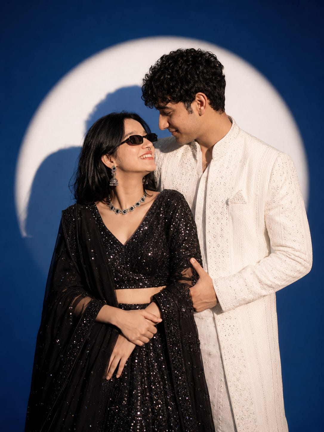 Indian couple in white sherwani and black sequin lehenga posing under a spotlight for a cinematic AI photo prompt