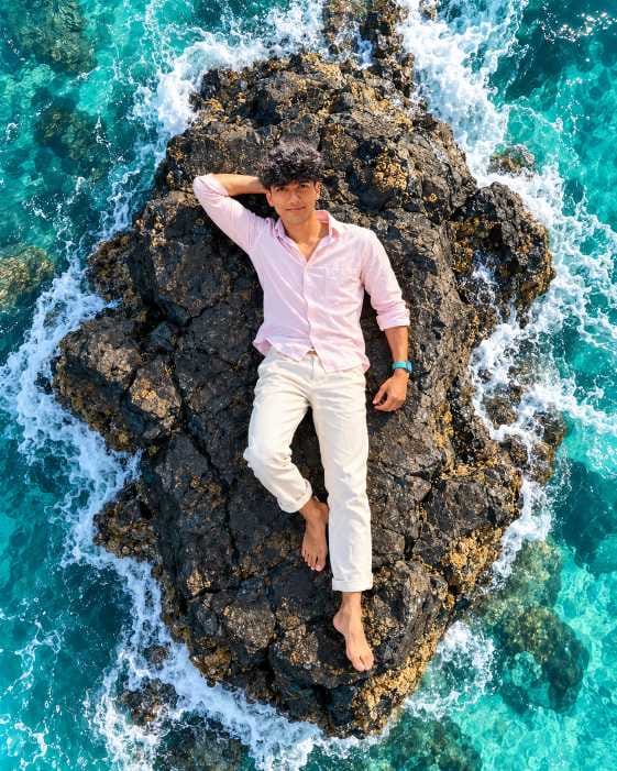 Drone view AI photo prompt for boys showing a boy lying on a rock with turquoise sea waves around