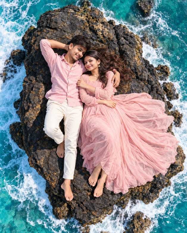 Drone view couple AI photo prompt showing a boy and a girl lying together on a rock surrounded by sea