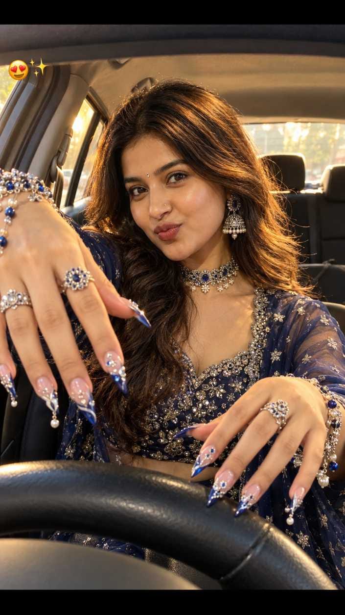 Woman sitting behind a car steering wheel with a playful pout, reaching hands forward, wearing navy outfit and silver jewelry